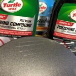 alt text: Close-up of a hand using a foam pad to apply polishing compound on a car's surface during scratch repair.