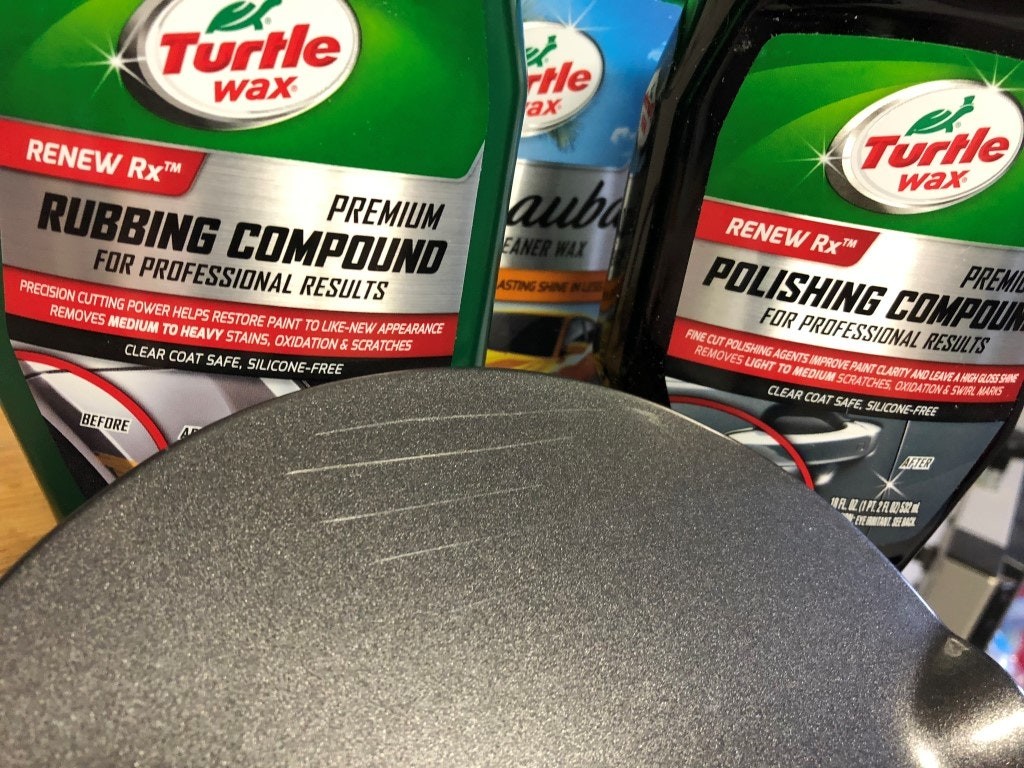 alt text: Close-up of a hand using a foam pad to apply polishing compound on a car's surface during scratch repair.
